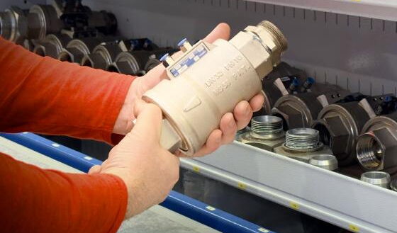 Person in rotem Pullover hält ein beigefarbenes Ventil mit blauen und weißen Markierungen in den Händen