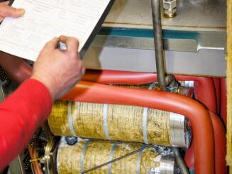 Person in rotem Hemd hält Klemmbrett mit Dokumenten über isolierten Rohren und Maschinenteilen